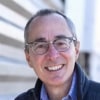 A smiling man in glasses with a warm and approachable expression.
