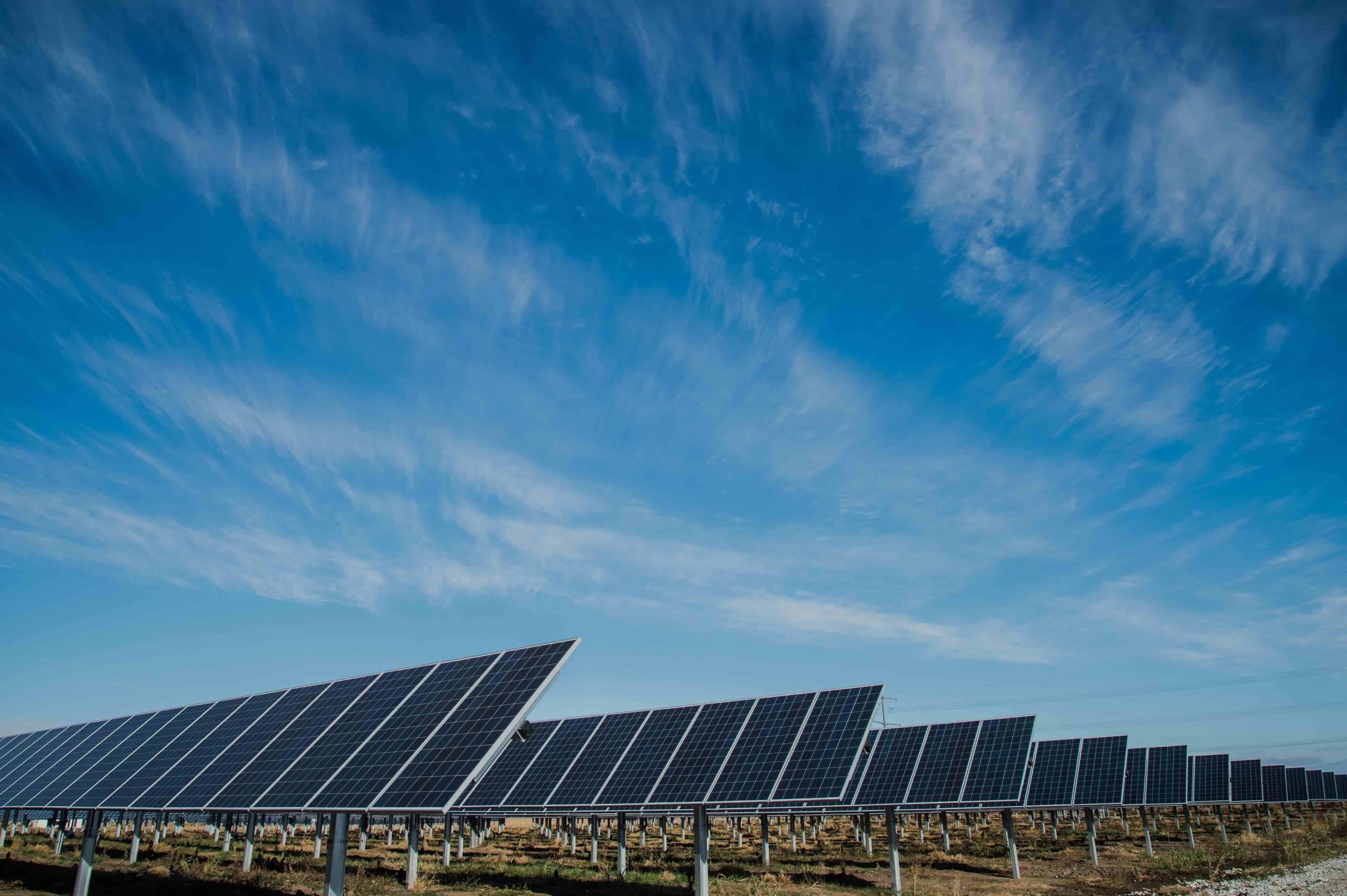 Rows of solar panels under a vast, cloudy blue sky, harnessing renewable energy from the sun.