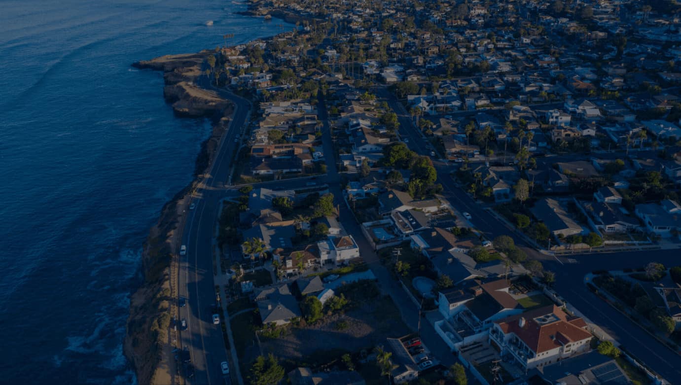 Aerial twilight view of a coastal town with streets and houses nestled by the sea.